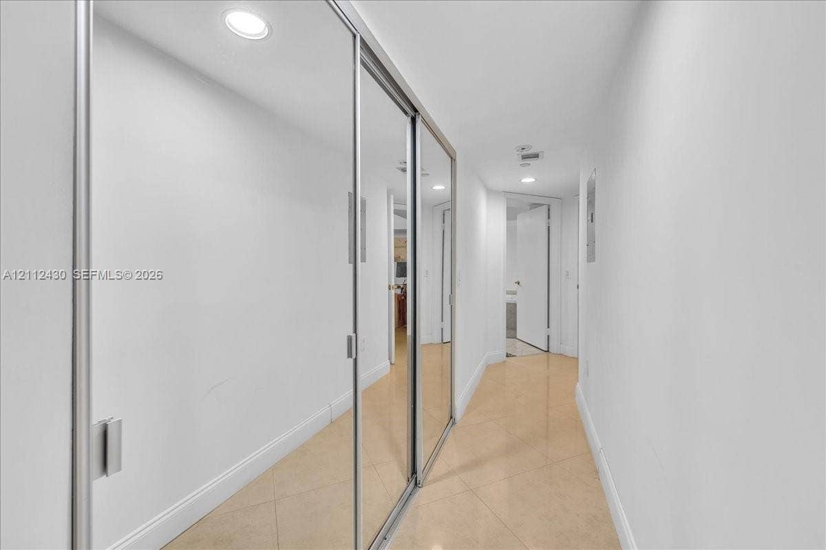 Hallway featuring floor-to-ceiling mirrored sliding closet doors, neutral tile flooring, and recessed lighting