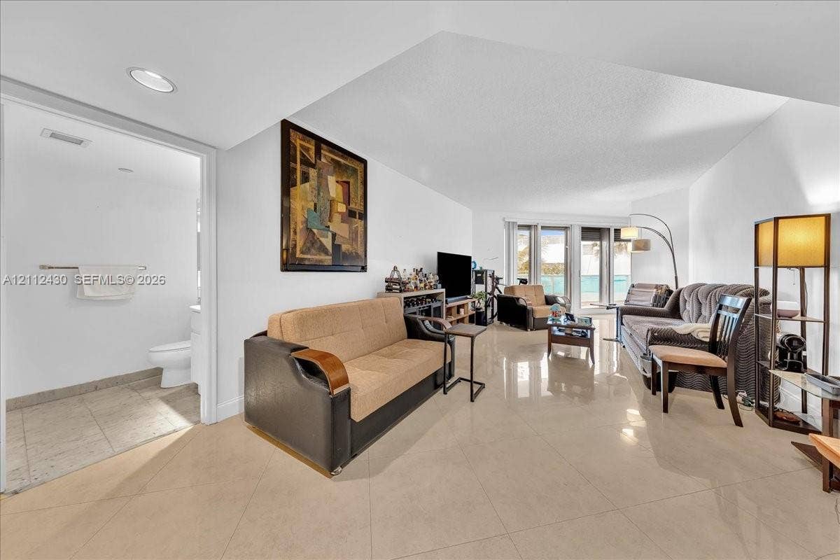 Open-concept interior featuring large-format tile flooring, recessed lighting, and a glass-paneled entry to an exterior space