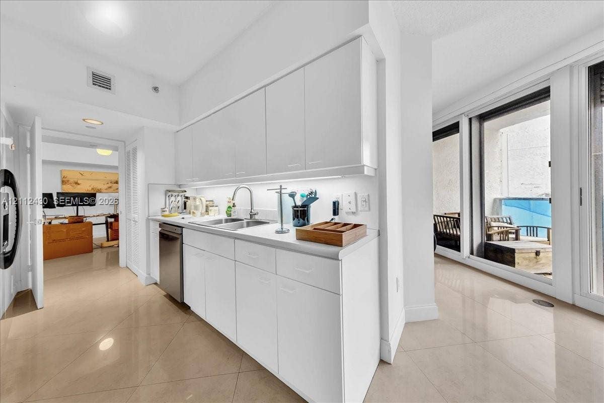 Kitchen featuring flat-panel high-gloss cabinetry, stone-finish countertops, stainless steel undermount sink, integrated stainless steel dishwasher, and polished tile flooring