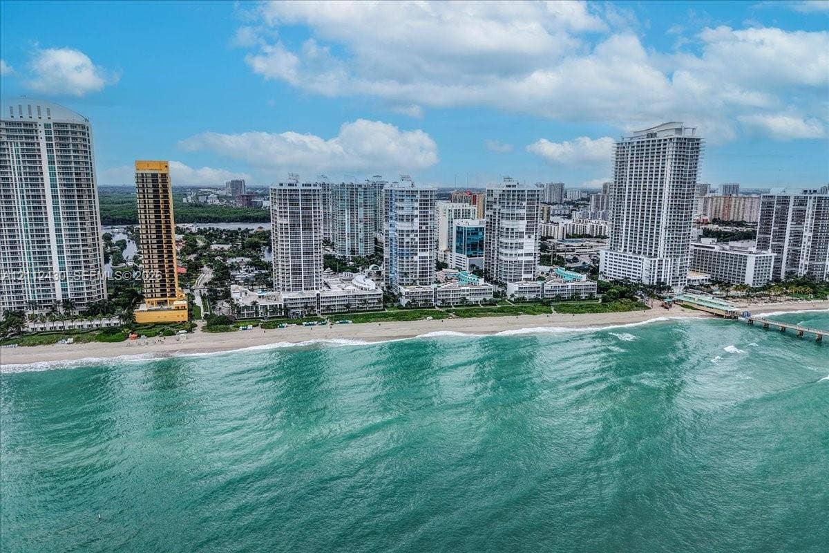 Aerial perspective of a high-rise residential corridor situated directly along the coastline, featuring expansive sandy beaches, deep-water ocean frontage, and established urban infrastructure