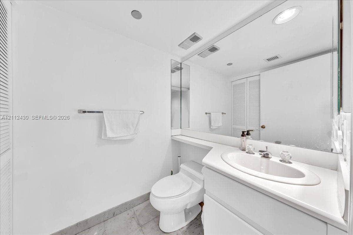 Vanity with an integrated sink and countertop, full-width wall mirror, and stone-finish flooring