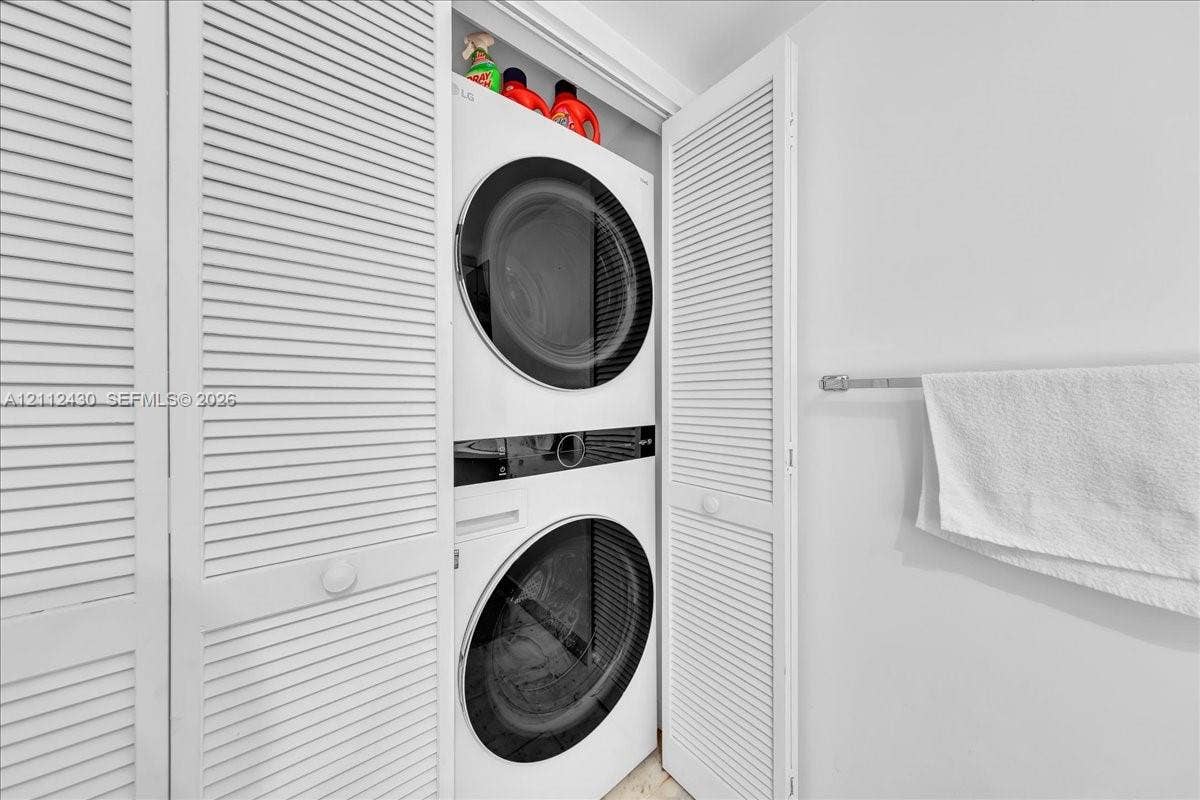 Stacked laundry unit with white finish, louvered closet doors, and horizontal metal wall-mounted towel bar