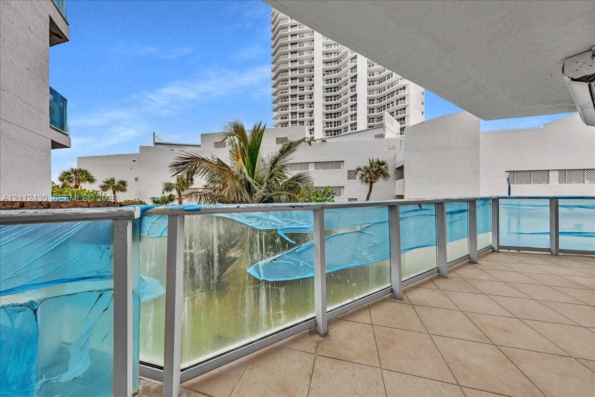 Covered balcony featuring tile flooring and a glass railing with metal framing
