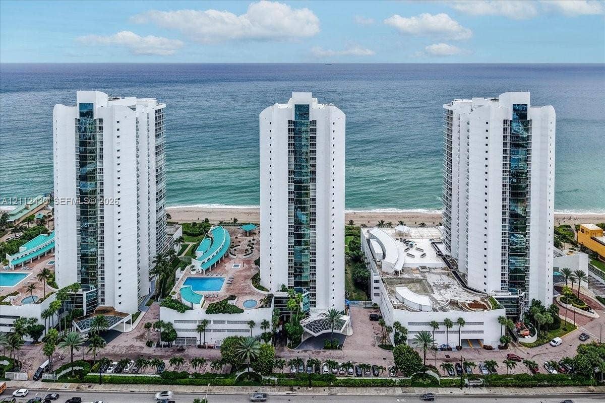 High-rise residential complex featuring oceanfront positioning, multiple swimming pools, tiered sun decks, and mature tropical landscaping