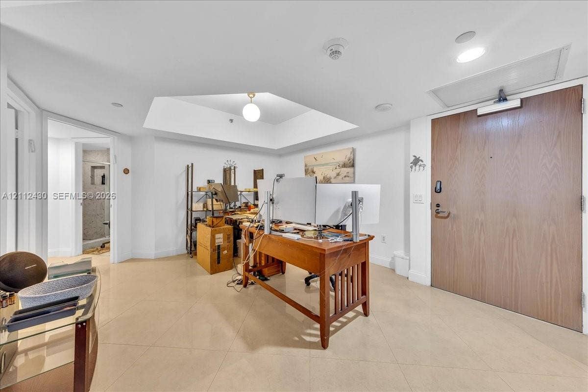 Large room featuring a coffered ceiling, recessed lighting, neutral tile flooring, and a solid wood entry door with a heavy-duty hydraulic door closer