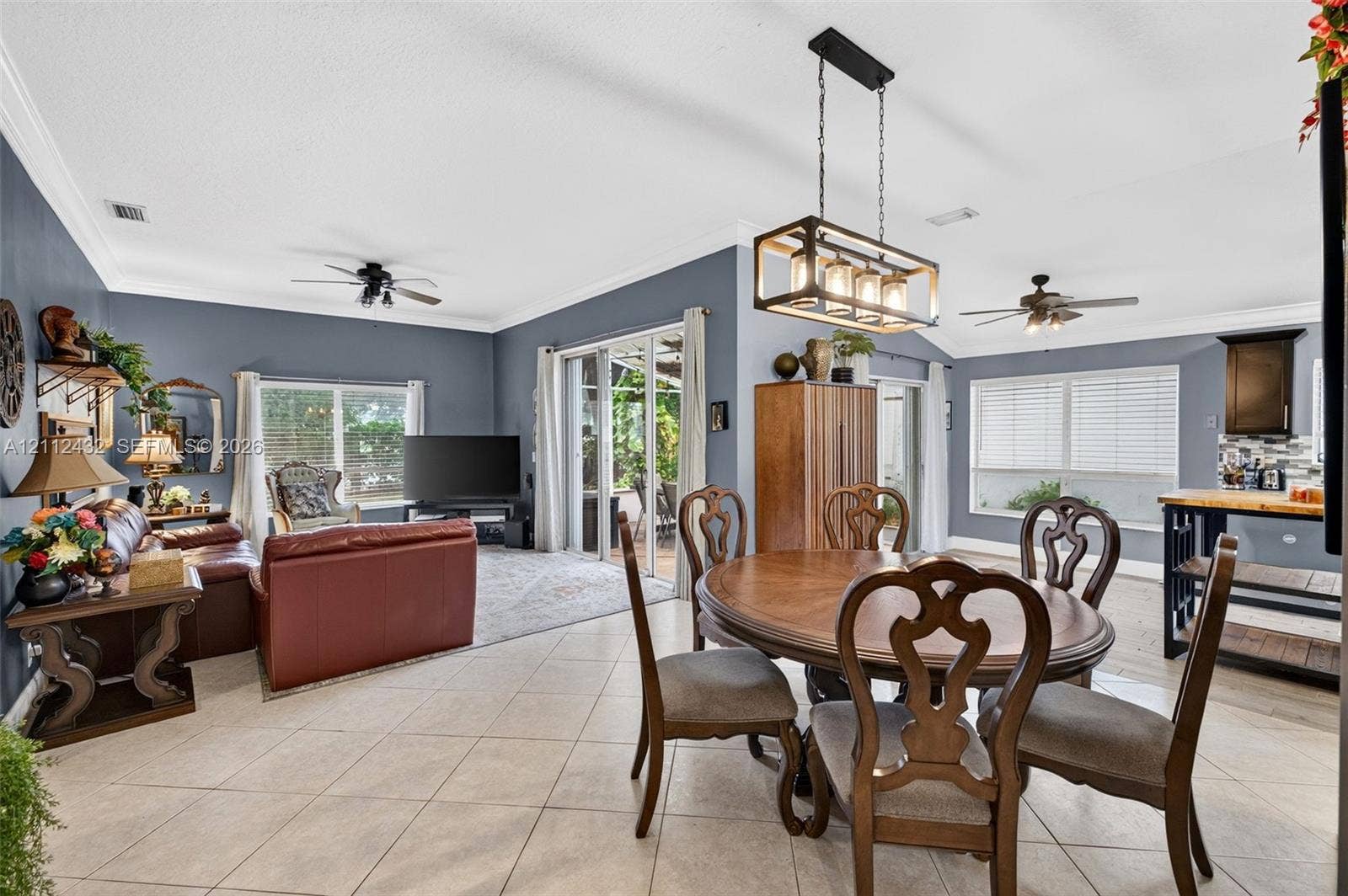 10545 NW 11th Court, Plantation, FL 33322 Open-concept main area featuring large-format ceramic tile flooring, crown molding, multi-light rectangular pendant fixture, dual ceiling fans, and multi-panel sliding glass doors
