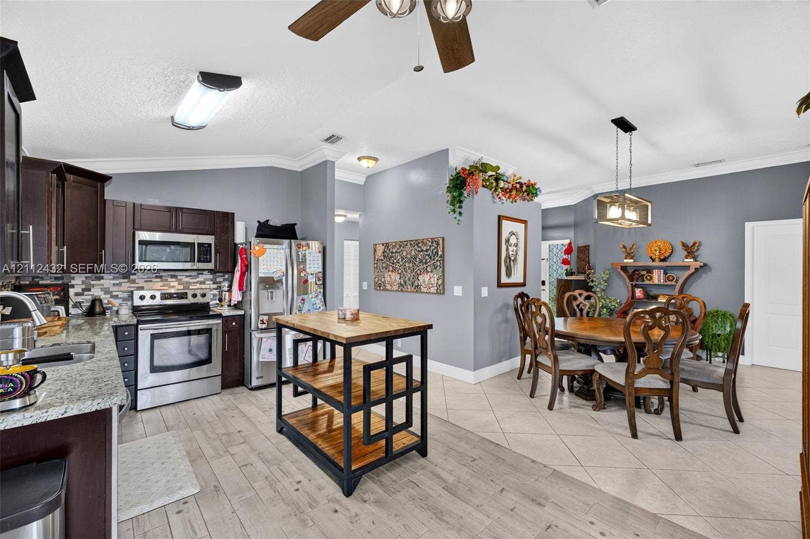 10545 NW 11th Court, Plantation, FL 33322 Kitchen featuring dark wood cabinetry, stainless appliances, multi-tonal tile backsplash, and granite-finish counters, accented by a pendant light fixture and wood-looktile flooring