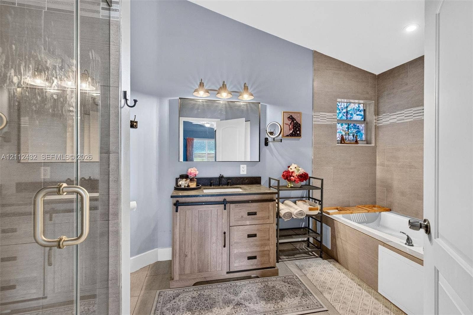 10545 NW 11th Court, Plantation, FL 33322 Bathroom featuring a wood-look vanity with a dark countertop, a glass-enclosed shower, a built-in soaking tub with tile surround, and a rectangular vanity mirror with integrated three-bulb lighting