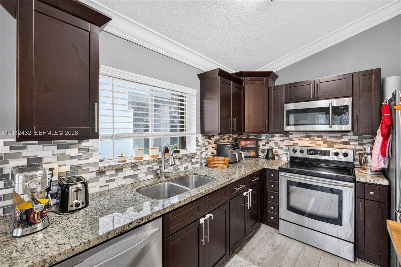 10545 NW 11th Court, Plantation, FL 33322 Kitchen featuring dark wood cabinetry, granite counters, stainless appliances, a multi-tone tile backsplash, and wood-look tile flooring