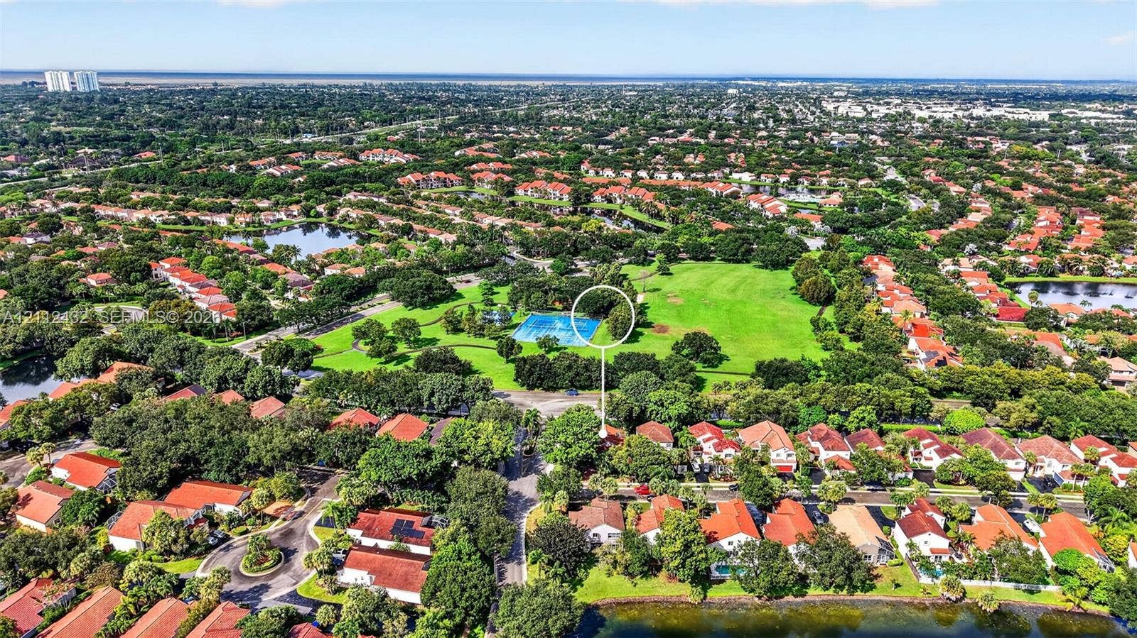 10545 NW 11th Court, Plantation, FL 33322 Aerial perspective featuring a residential property situated near an expansive green space, mature canopy trees, and community recreational court facilities