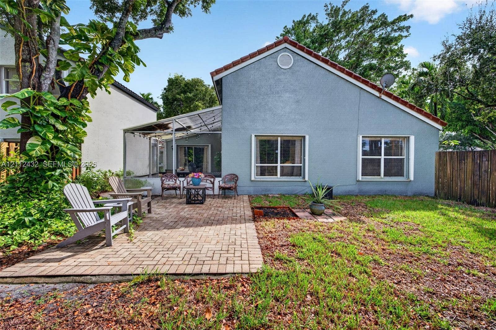 10545 NW 11th Court, Plantation, FL 33322 Rear exterior featuring a brick paver patio, screened-in enclosure, stucco siding, and a gabled roof