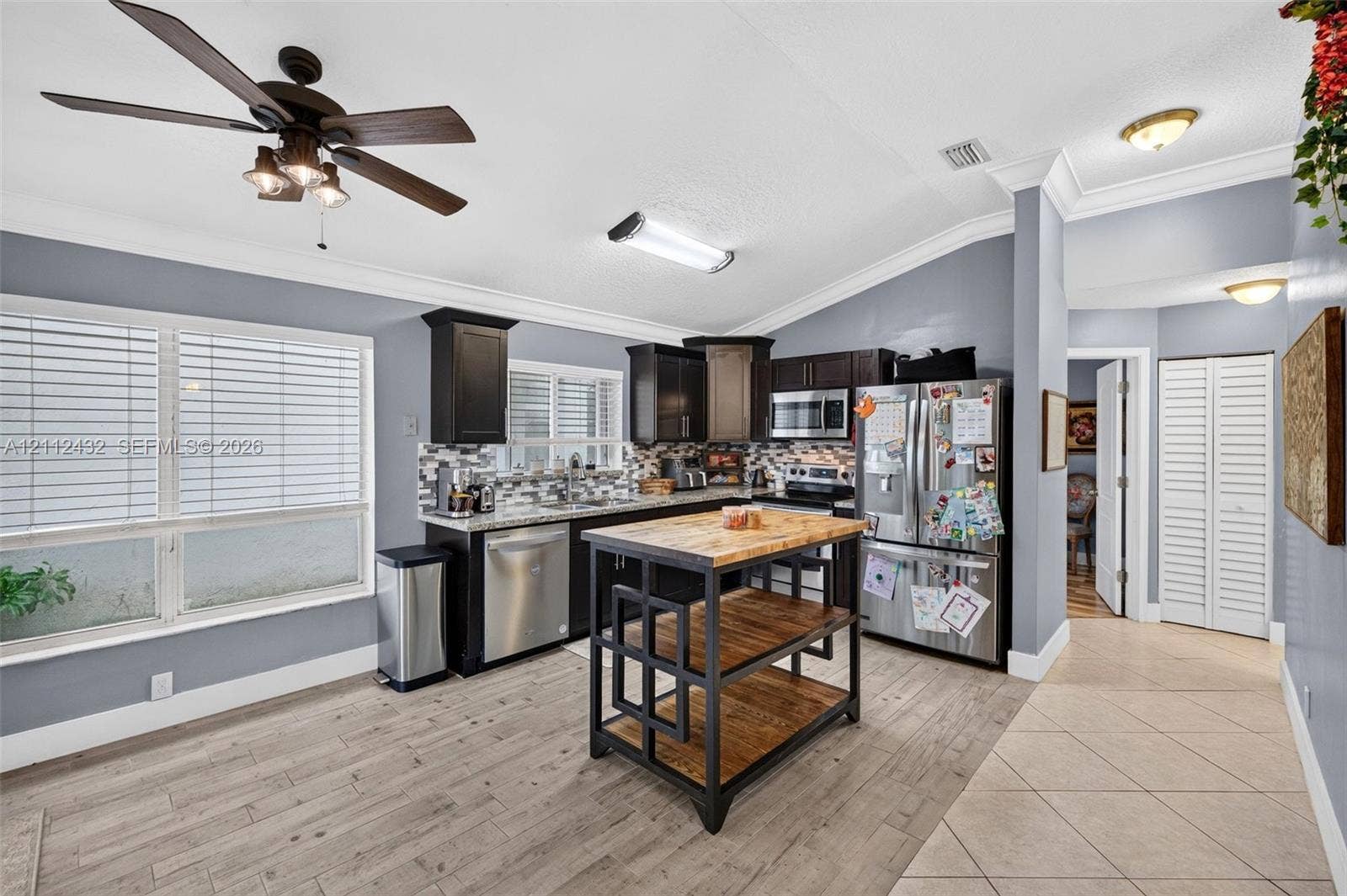 10545 NW 11th Court, Plantation, FL 33322 Kitchen featuring dark-toned cabinetry, stainless appliances, patterned backsplash, wood-look tile flooring, and crown molding