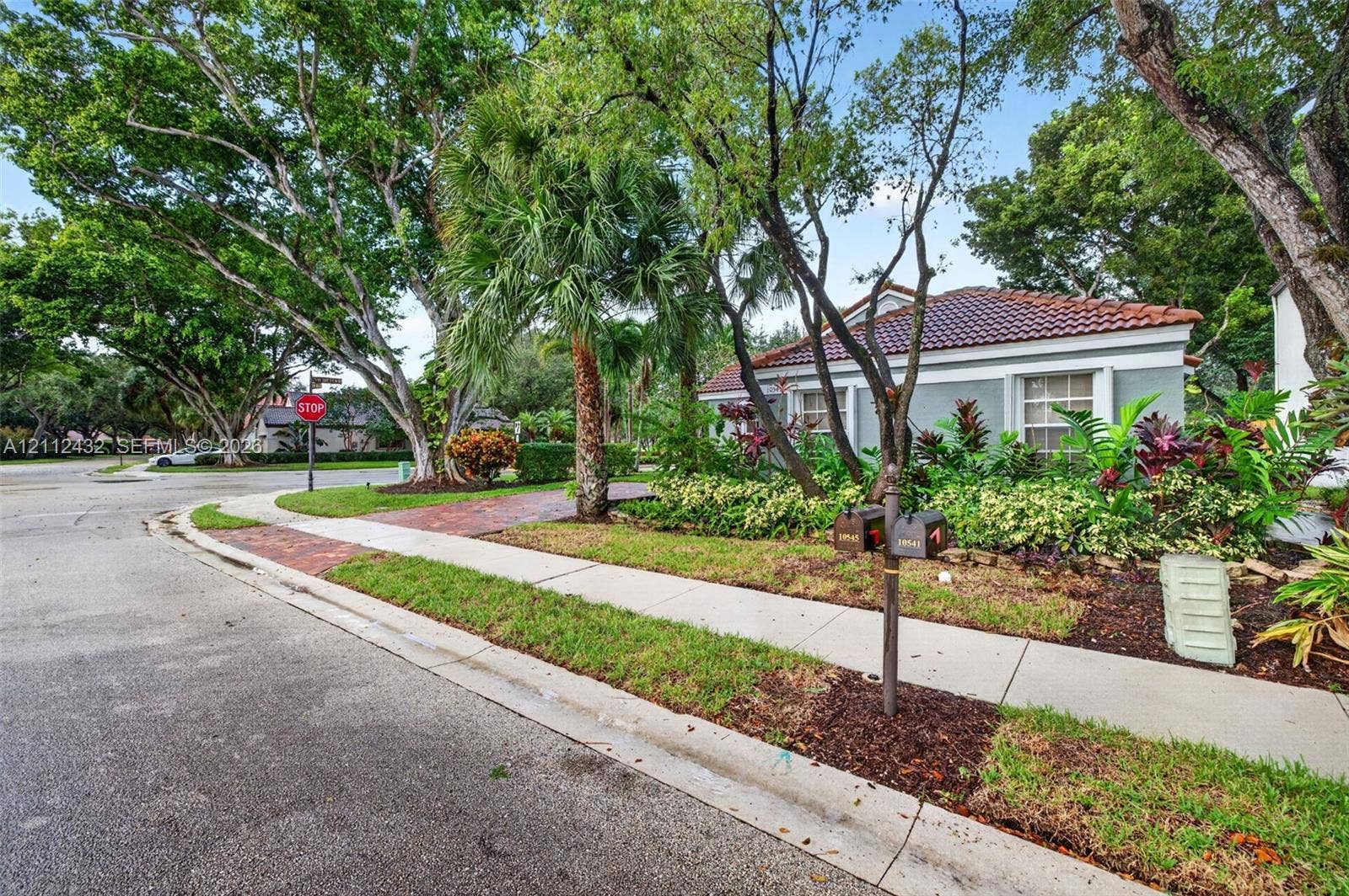 10545 NW 11th Court, Plantation, FL 33322 Exterior featuring a tile roof, brick-paved driveway, mature landscaping, and established trees