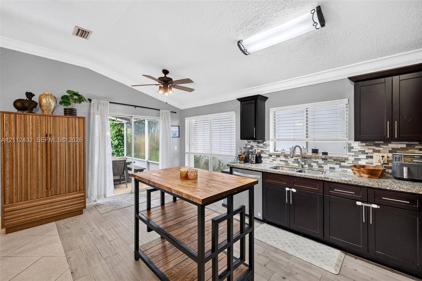 10545 NW 11th Court, Plantation, FL 33322 Kitchen featuring dark cabinetry, granite-finish countertops, tile backsplash, wood-look tile flooring, and a center island cart with a wood surface