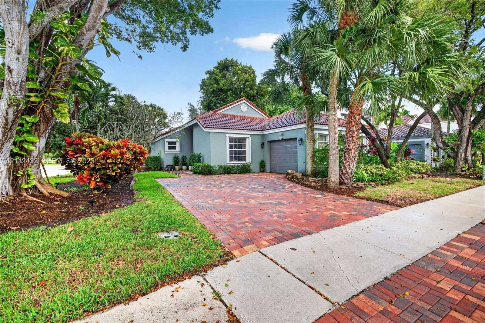 10545 NW 11th Court, Plantation, FL 33322 Single-story home featuring a 2015 tile roof, 2025 paver driveway, attached garage, and beautiful established landscaping with mature palm trees