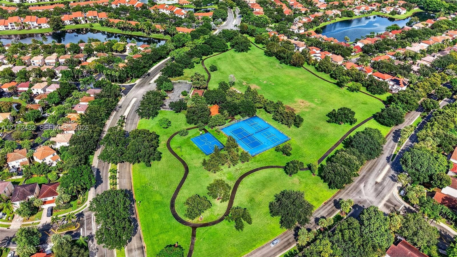 10545 NW 11th Court, Plantation, FL 33322 Expansive green space featuring tennis courts, a basketball court, mature trees, and paved walking paths