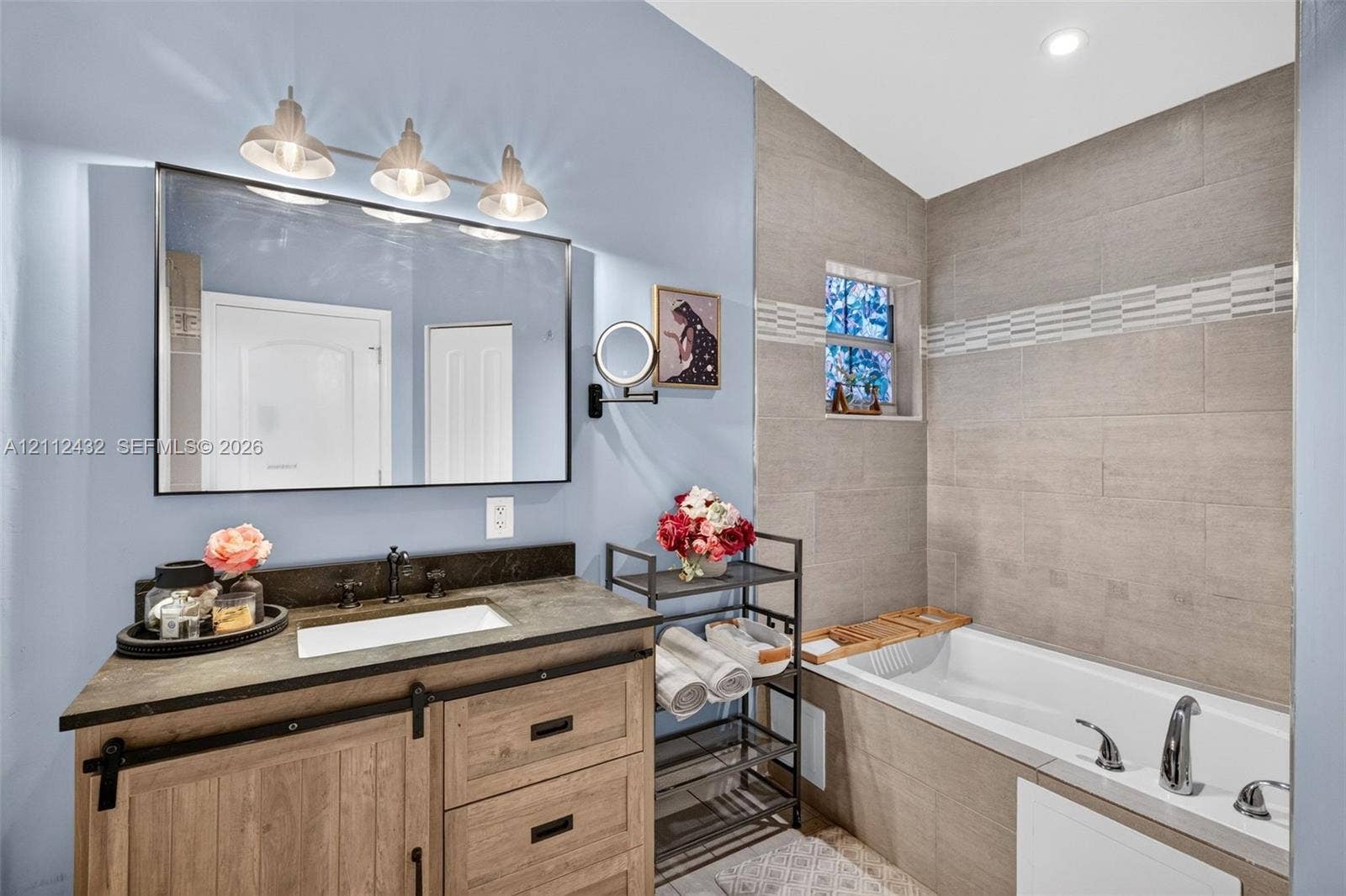 10545 NW 11th Court, Plantation, FL 33322 Wood-look vanity with a dark counter and rectangular drop-in sink, framed mirror with three-bulb vanity lighting, and a bathtub with tile surround and separate shower