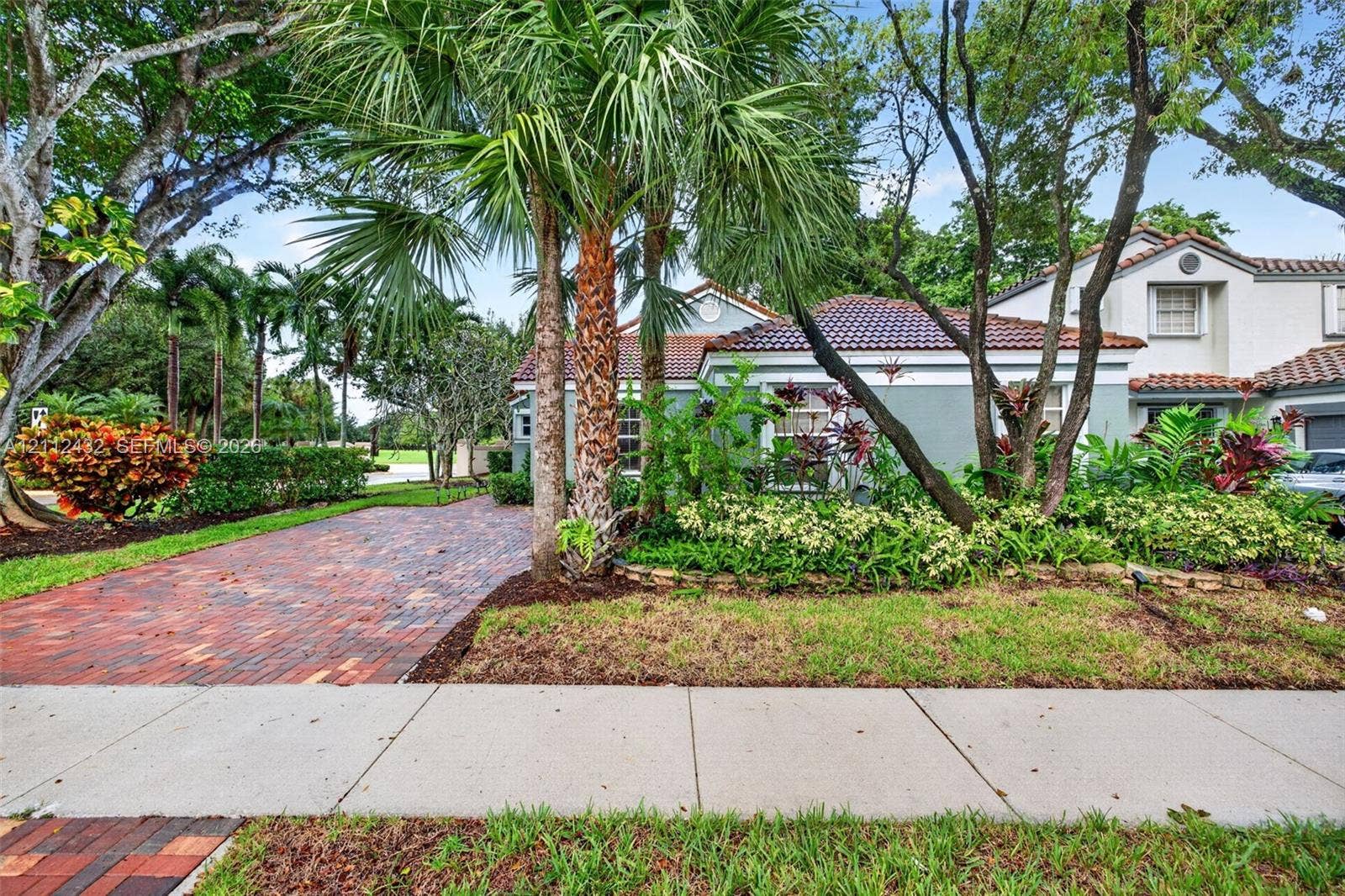 10545 NW 11th Court, Plantation, FL 33322 Exterior featuring a multi-toned brick paver driveway, clay tile roof, and mature tropical landscaping