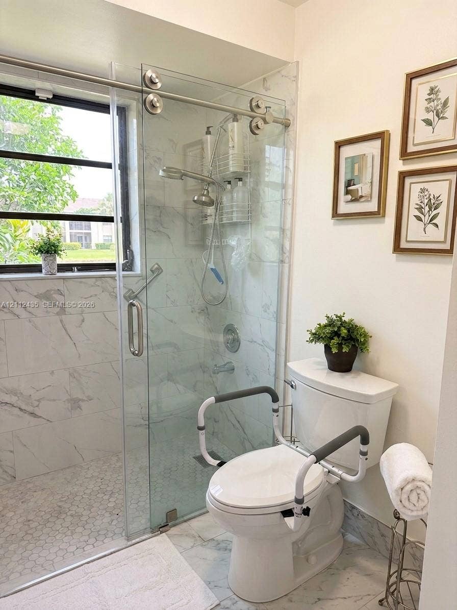 8810 SW 123rd Court, #M103, Miami, FL 33186 Walk-in shower featuring a sliding glass door, white stone-finish tile surround, hexagon floor tile, and chrome fixtures