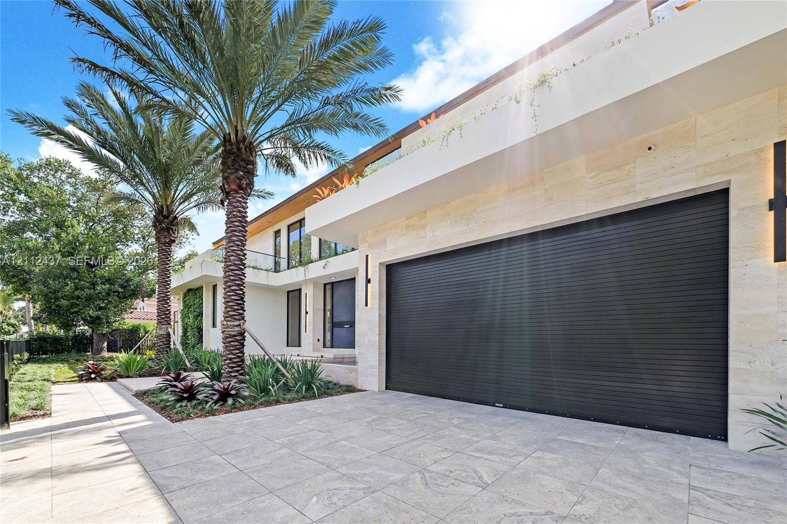 770 Lake Road, Miami, FL 33137 Modern exterior featuring stone facade cladding, large-format paved driveway, sleek roll-down garage door, and glass balcony railings