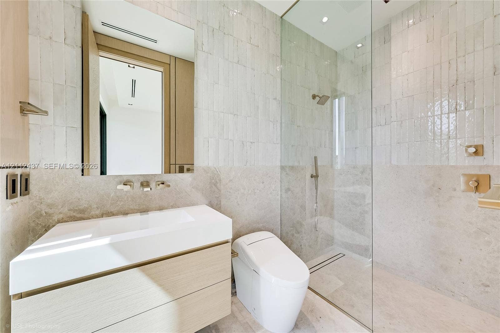 770 Lake Road, Miami, FL 33137 Floating vanity with integrated sink, glass-enclosed walk-in shower, wall-mounted brushed metal plumbing fixtures, and textured stone wall tile