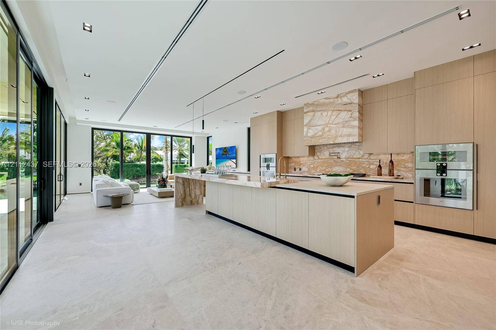 770 Lake Road, Miami, FL 33137 Floor-to-ceiling retractable glass walls, light wood-paneled ceiling with integrated recessed lighting, expansive stone flooring, and custom built-in shelving