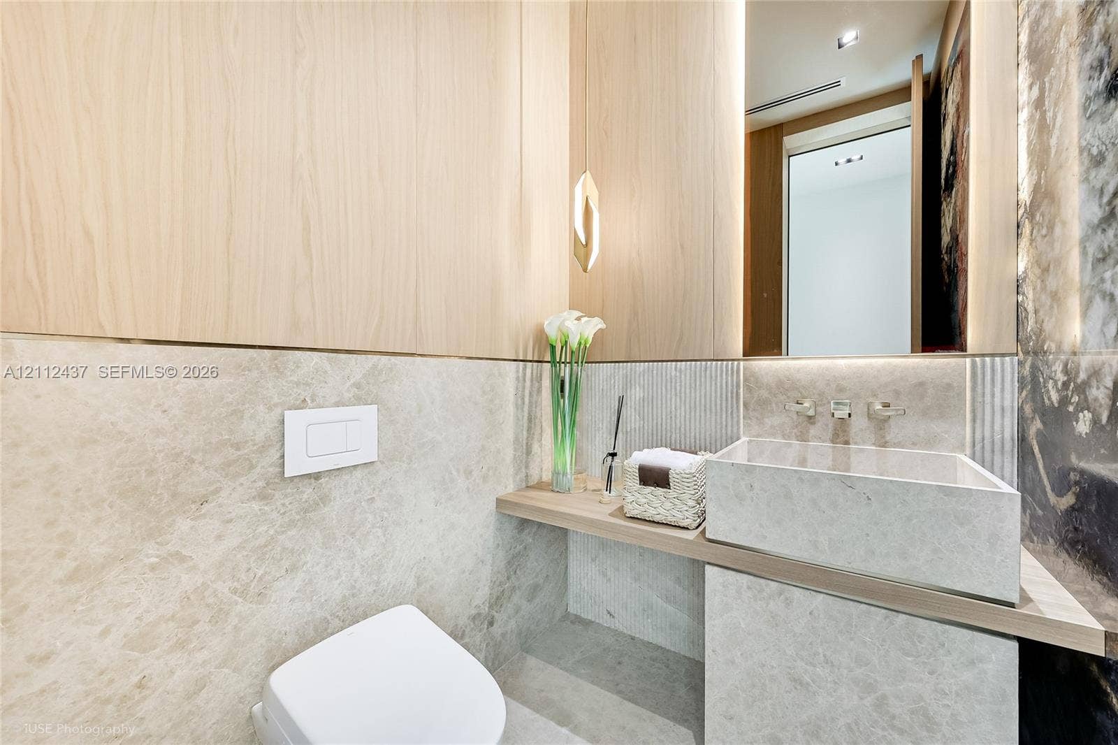 770 Lake Road, Miami, FL 33137 Wall-mounted toilet with a concealed flush plate, stone-tiled walls, light wood paneling, stone vanity with a vessel sink, and integrated LED accent lighting