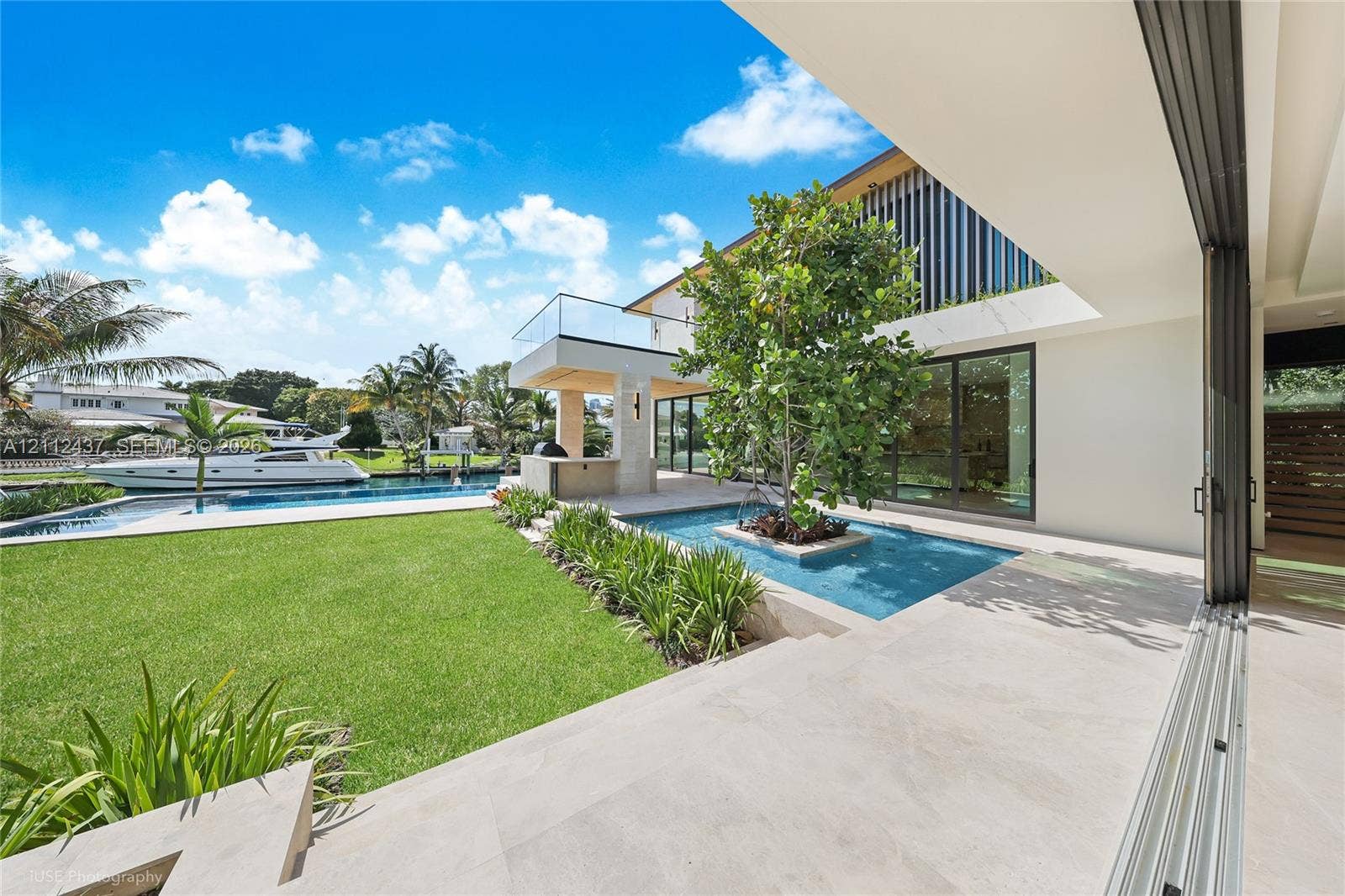770 Lake Road, Miami, FL 33137 Outdoor terrace featuring a reflective water feature with a central tree, built-in stone kitchen, glass-railed balcony, and retractable wall panels