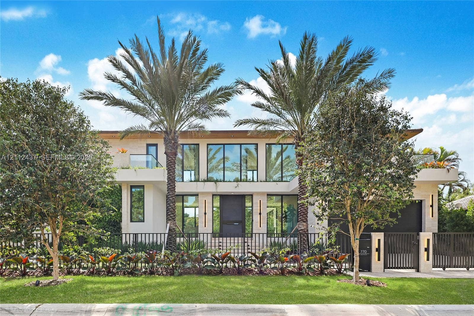 770 Lake Road, Miami, FL 33137 Contemporary two-story exterior featuring smooth stucco facade, floor-to-ceiling glass windows, integrated wall-mounted lighting, manicured landscaping, and decorative metal fencing