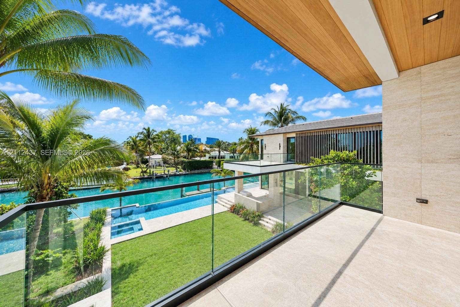 770 Lake Road, Miami, FL 33137 Covered balcony featuring stone flooring, wood-plank ceiling, and a frameless glass railing overlooking the waterfront property, swimming pool, and landscaped lawn
