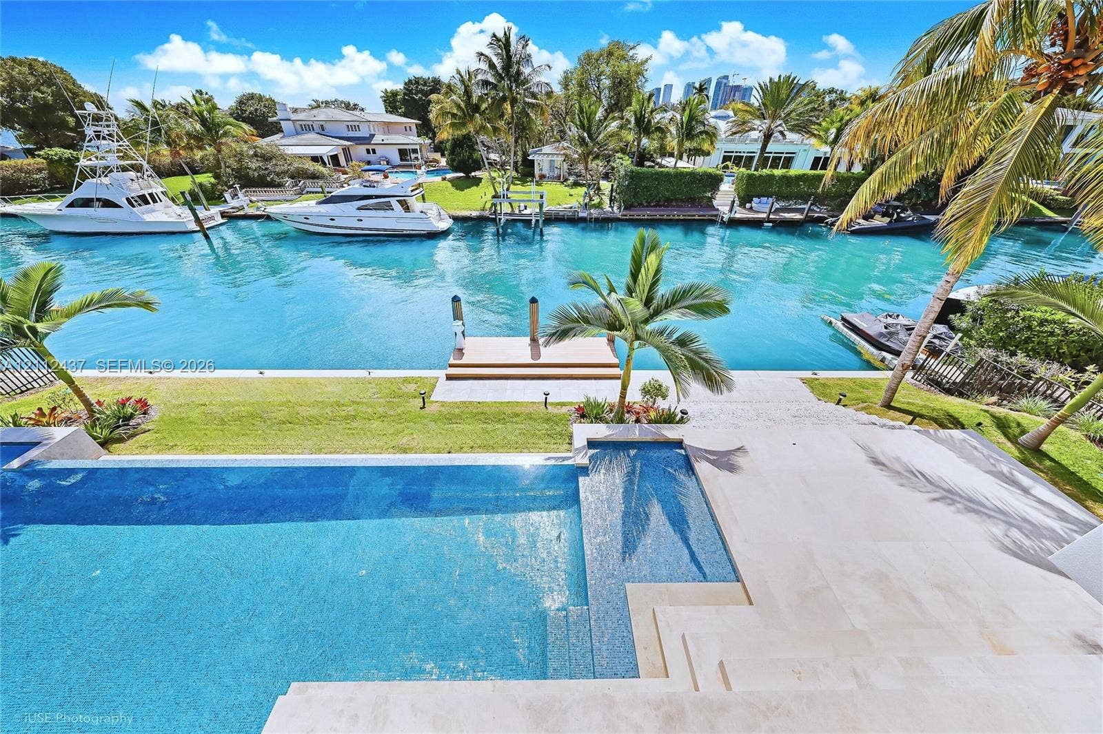 770 Lake Road, Miami, FL 33137 Waterfront estate featuring a paved terrace, swimming pool with integrated sun shelf, private boat dock, and manicured landscaping