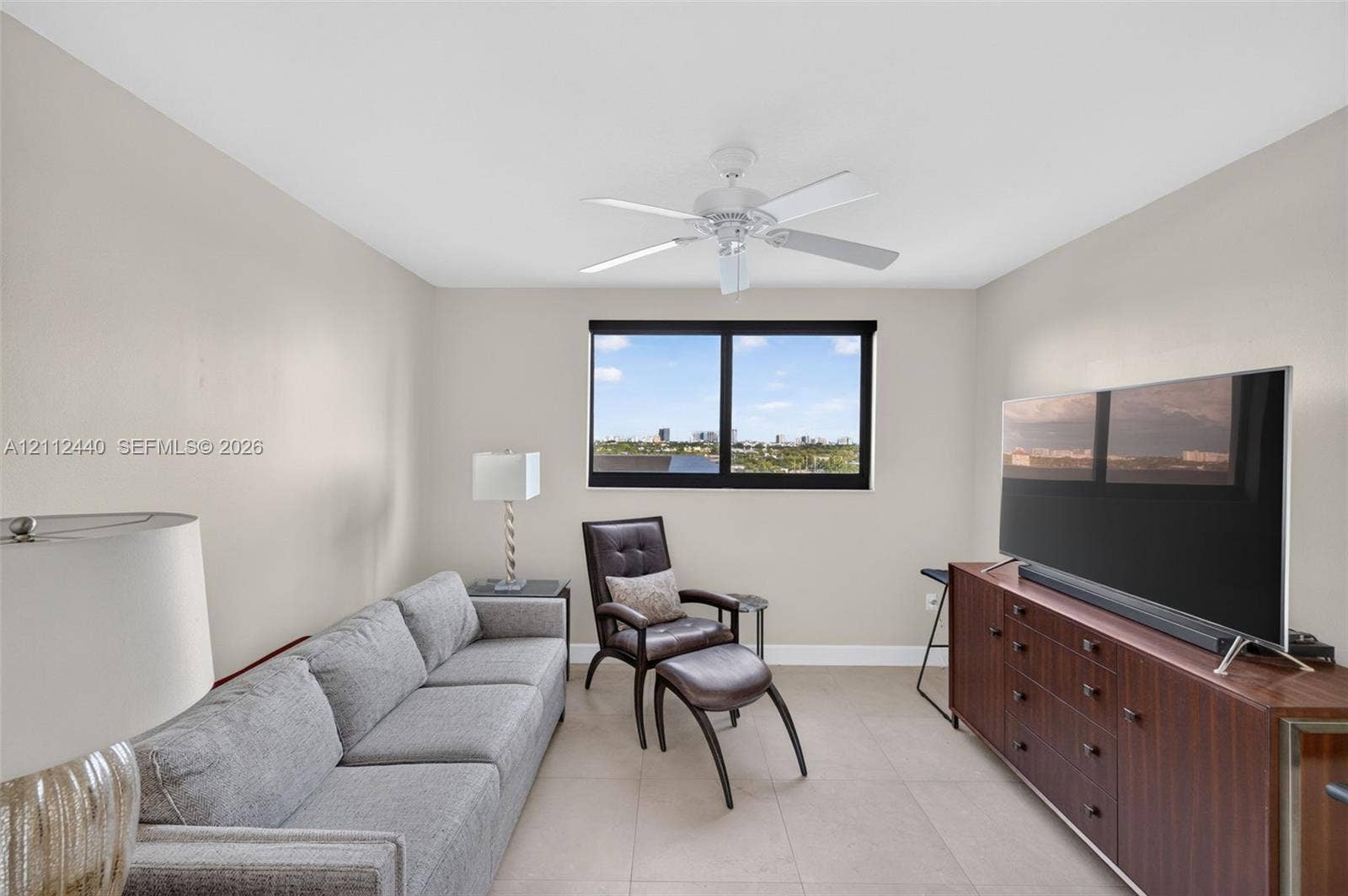 110 N Federal Highway, #914, Fort Lauderdale, FL 33301 Neutral-toned guest bedroom featuring large-format porcelain flooring, a central ceiling fan with integrated lighting, and impact window with motorized roller shade