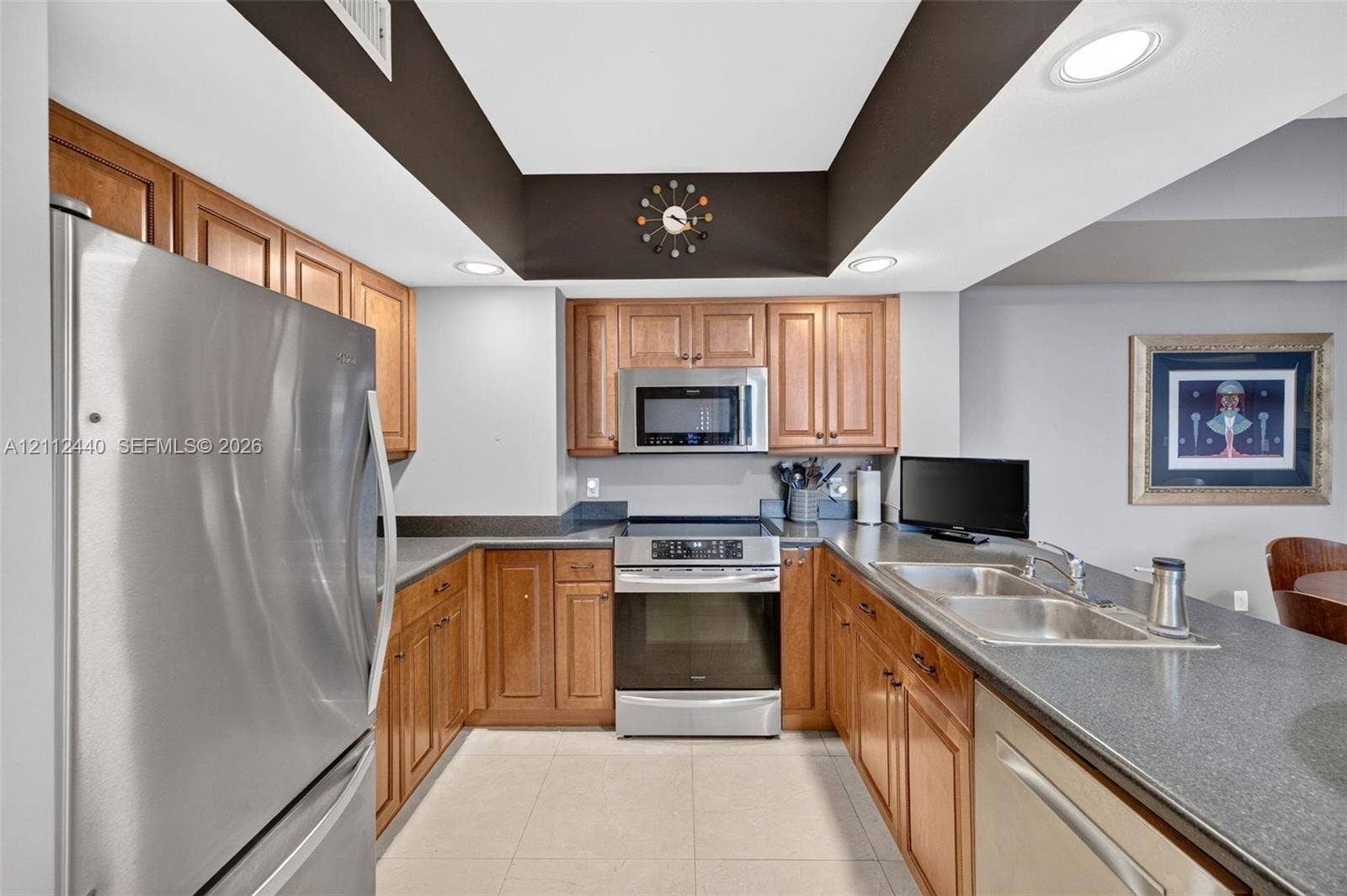 110 N Federal Highway, #914, Fort Lauderdale, FL 33301 Kitchen featuring recessed tray ceiling, wood cabinetry, stainless appliances, dual-basin stainless steel sink, and dark countertops