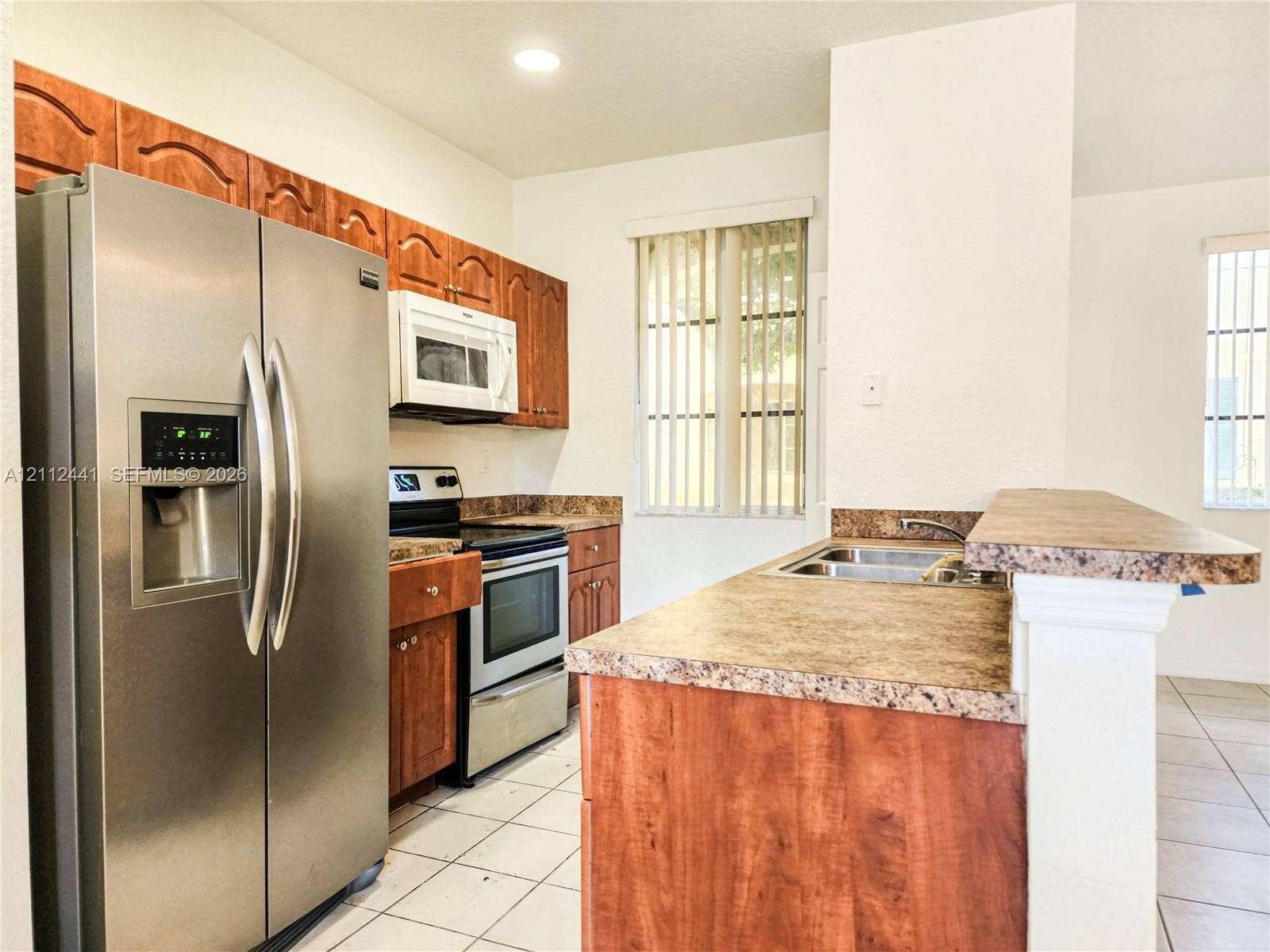 Kitchen featuring stainless steel appliances, wood cabinetry, patterned laminate countertops, a dual-basin sink, and tile flooring