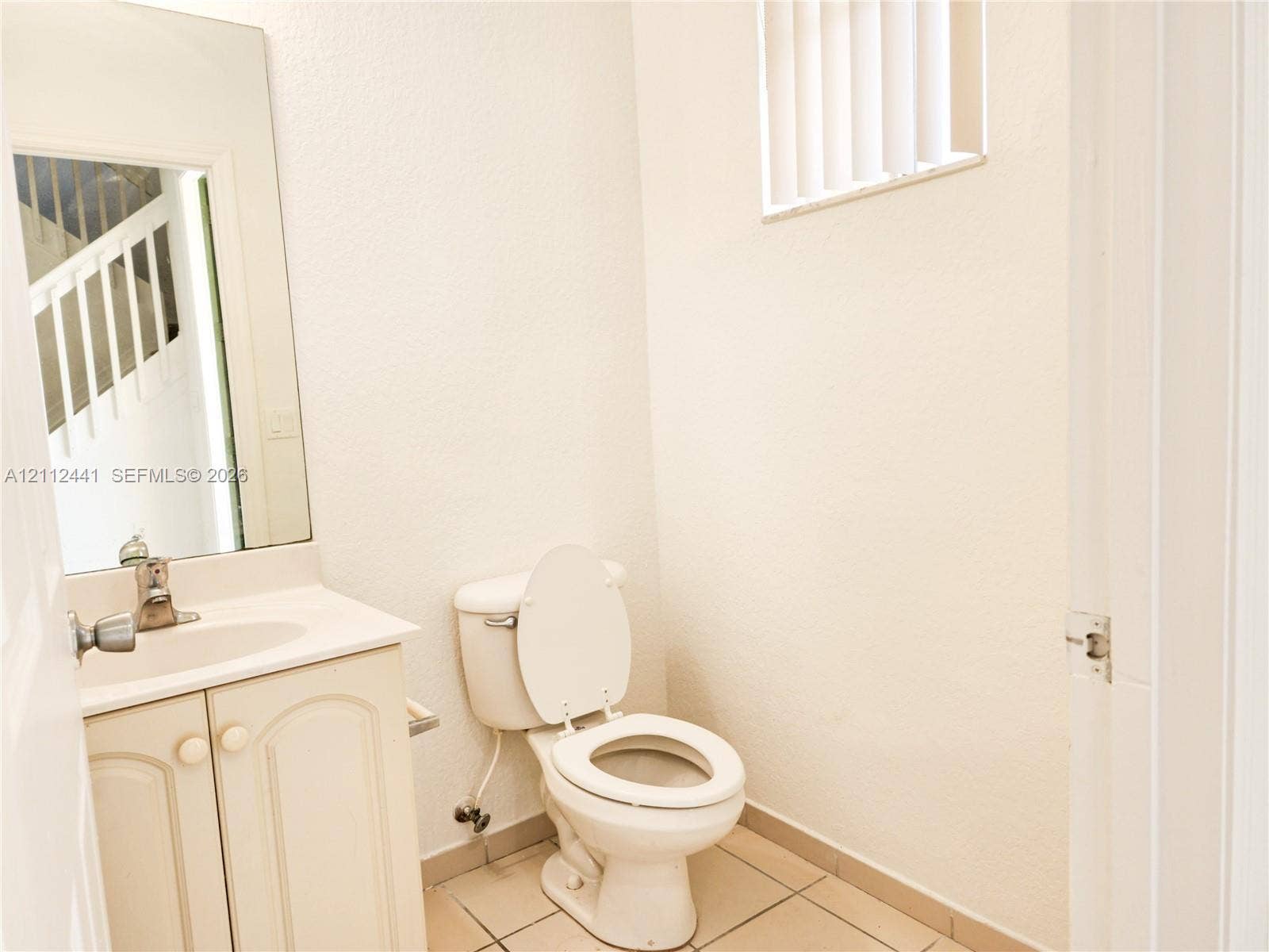 Vanity featuring cabinet storage and a sink basin, white toilet, wall-mounted mirror, and tile flooring