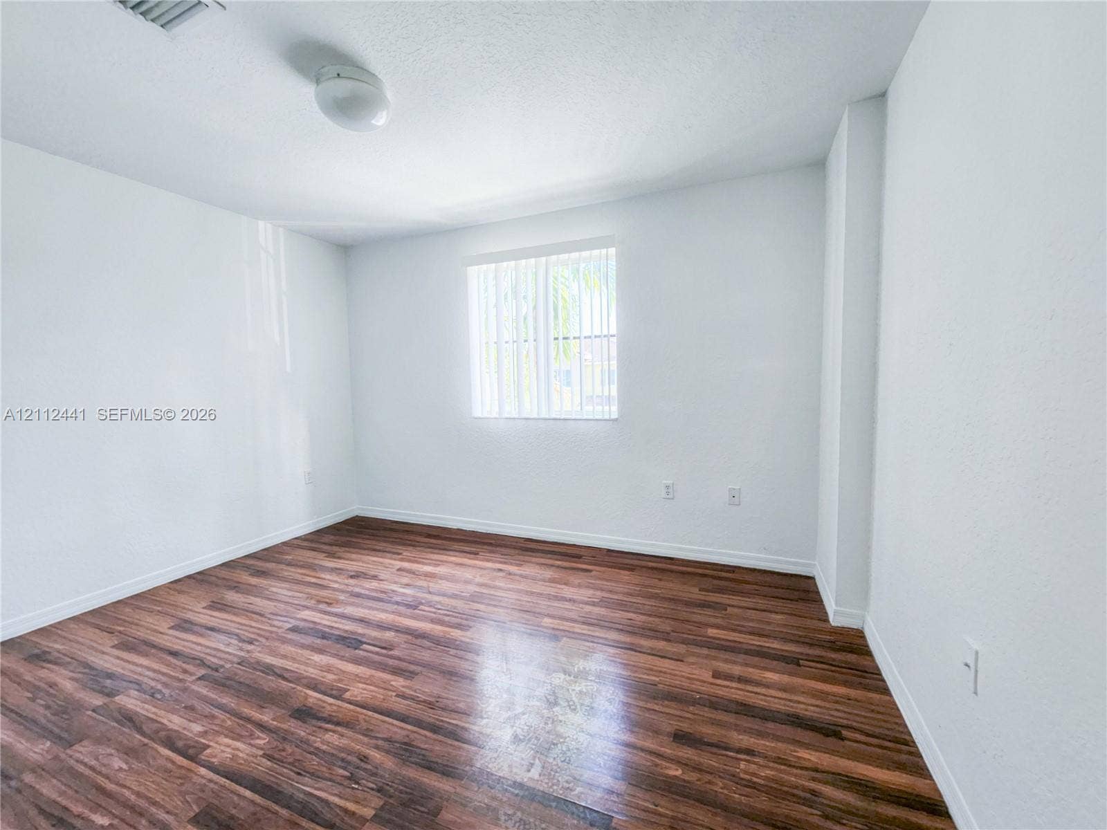 Room featuring wood-finish flooring, white walls, and a single window with vertical blinds