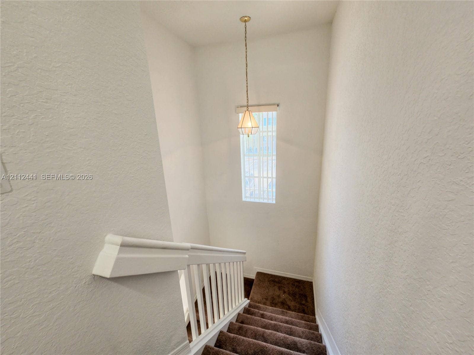 Stairwell featuring carpeted steps, white baluster railing, and a geometric pendant light fixture