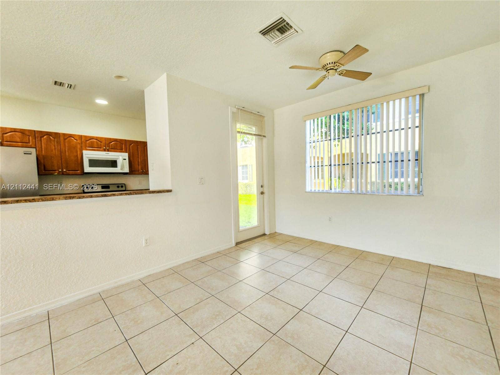 Kitchen area featuring wood cabinetry, stone-finish countertops, stainless steel appliances, neutral tile flooring, and a ceiling fan