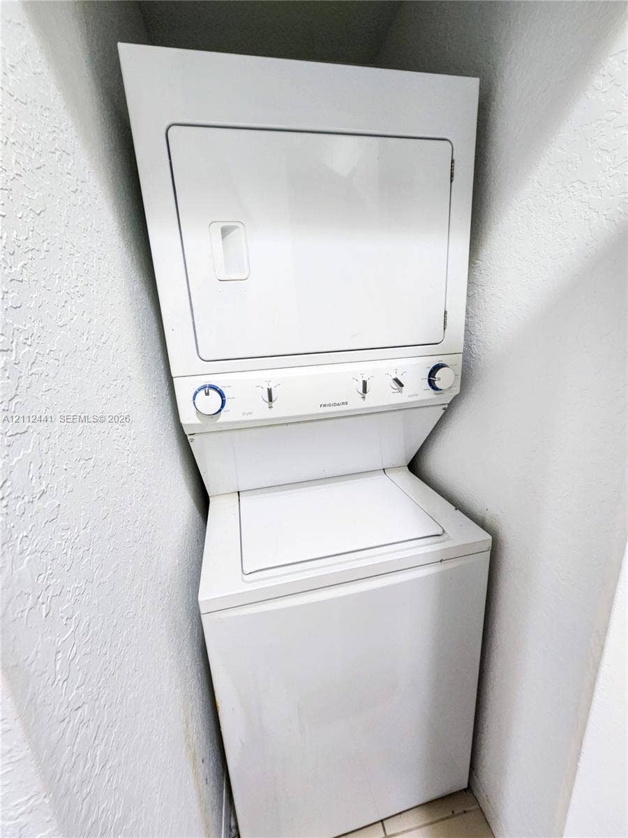 Stacked white laundry appliance featuring a top-loading washer and a dryer with manual rotary control dials