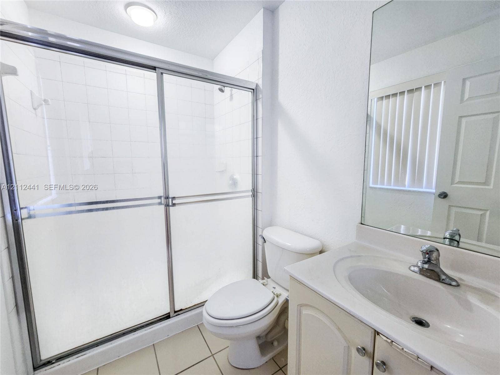 Bathroom featuring a walk-in shower with sliding glass doors, white tile surround, vanity with an integrated sink, and a wall-mounted mirror