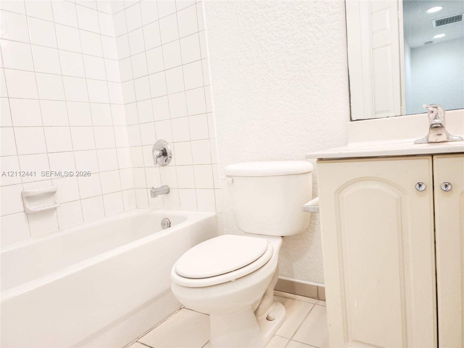 Bathroom featuring a white vanity cabinet with an integrated sink and chrome faucet, a bathtub with a white tile surround, and a wall-mounted mirror
