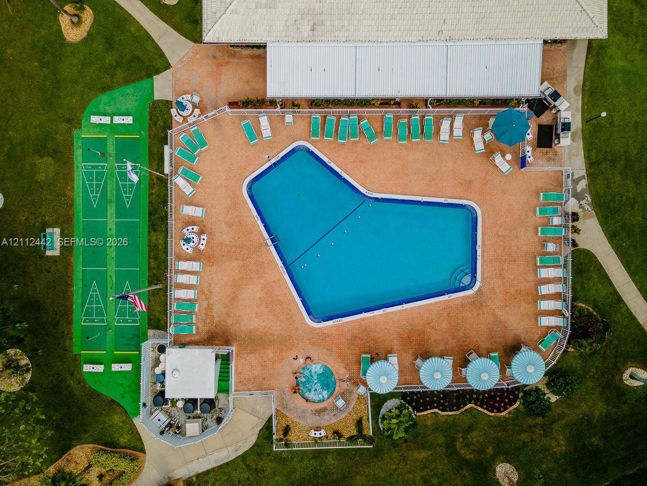2455 NE 51st Street, #E114, Fort Lauderdale, FL 33308 Aerial view featuring an expansive swimming pool, an integrated circular spa, a dual-lane shuffleboard court, a concrete pool deck, and a fenced perimeter