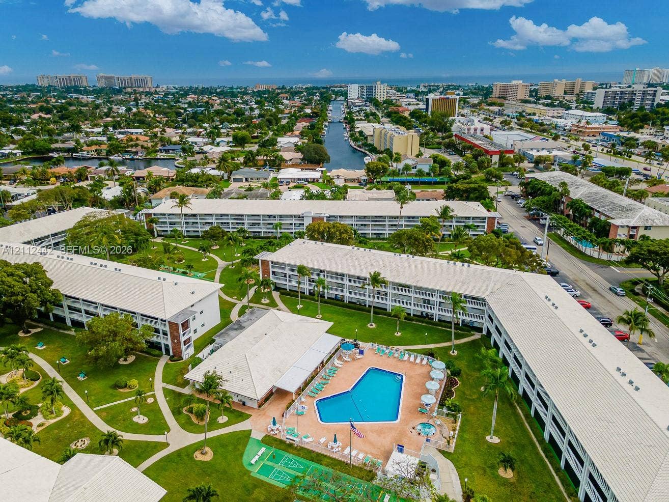2455 NE 51st Street, #E114, Fort Lauderdale, FL 33308 Multi-story residential complex featuring a central outdoor swimming pool, spa, manicured landscaping, paved walkways, and a dedicated shuffleboard court