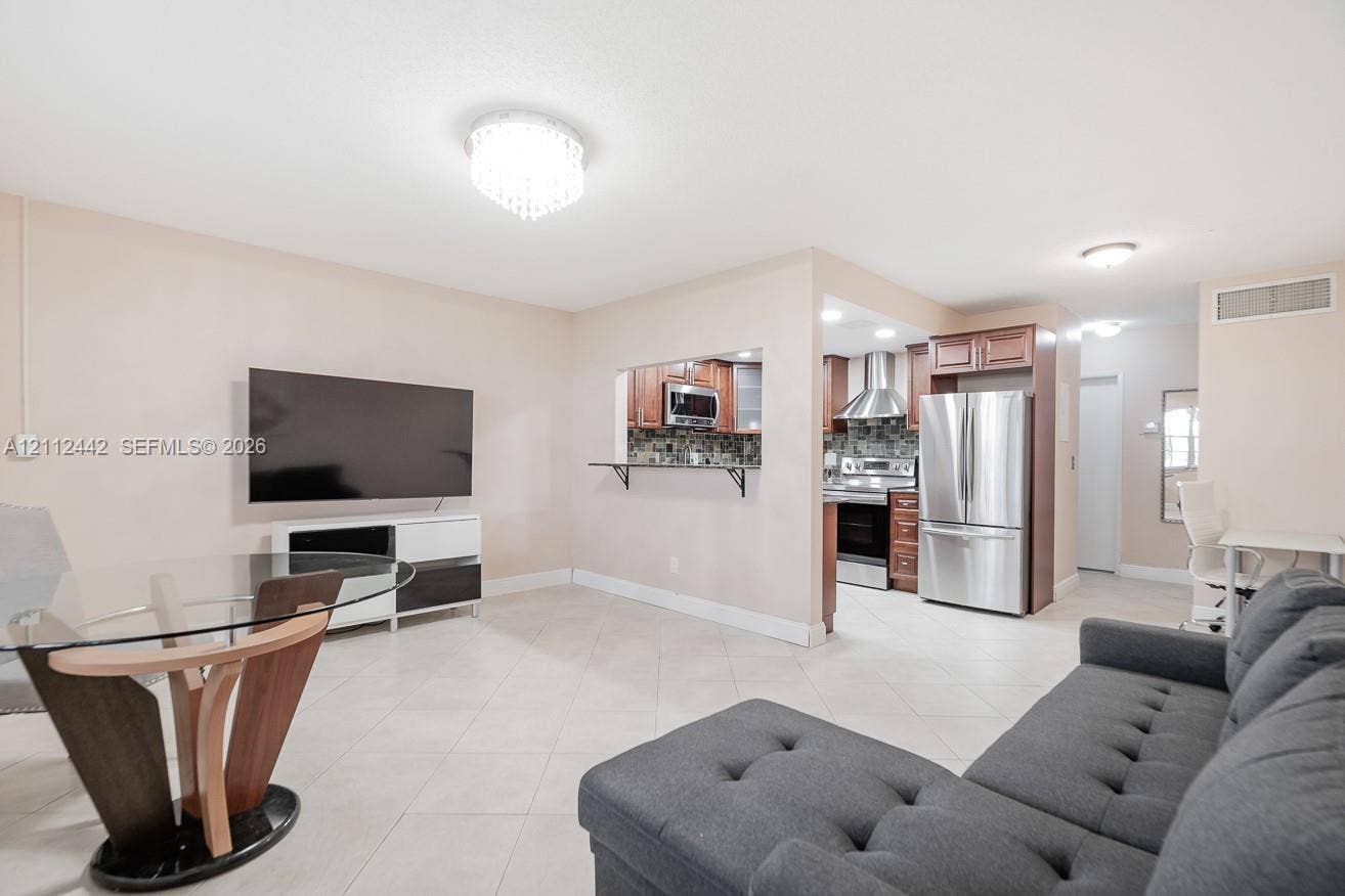 2455 NE 51st Street, #E114, Fort Lauderdale, FL 33308 Open-concept living space featuring ceramic tile flooring, built-in breakfast bar pass-through, stainless steel kitchen appliances, and decorative flush-mount ceiling lighting
