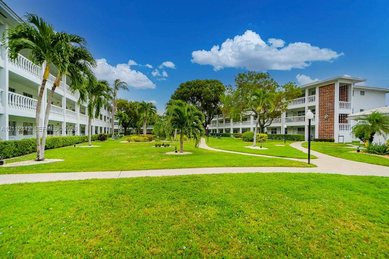 2455 NE 51st Street, #E114, Fort Lauderdale, FL 33308 Expansive central courtyard featuring manicured lawn, paved walkways, mature palm trees, and multi-story buildings with white balcony railings