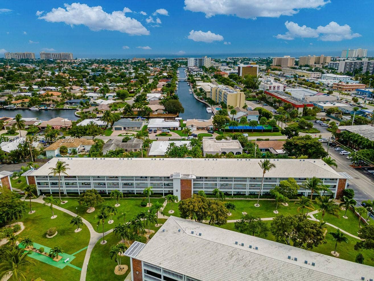 2455 NE 51st Street, #E114, Fort Lauderdale, FL 33308 Aerial perspective of a multi-story residential building featuring exterior corridors, a metal roof, landscaped grounds, winding concrete walkways, and a miniature putting green