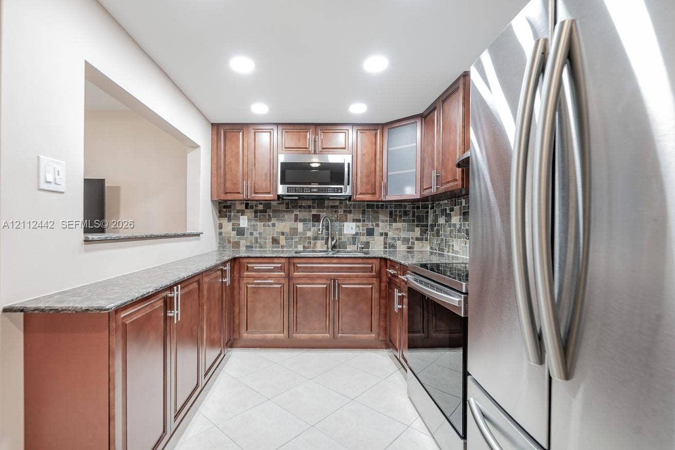 2455 NE 51st Street, #E114, Fort Lauderdale, FL 33308 Kitchen featuring stained wood cabinetry, stone-finish countertops, mosaic tile backsplash, recessed lighting, and stainless steel appliances
