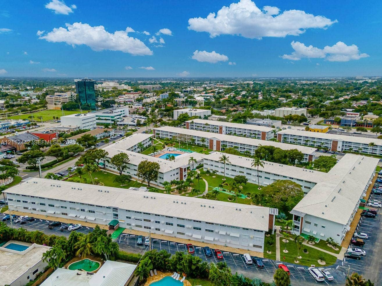 2455 NE 51st Street, #E114, Fort Lauderdale, FL 33308 Aerial perspective of a multi-building residential complex featuring a central courtyard, landscaped green space, an outdoor swimming pool, and dedicated parking areas