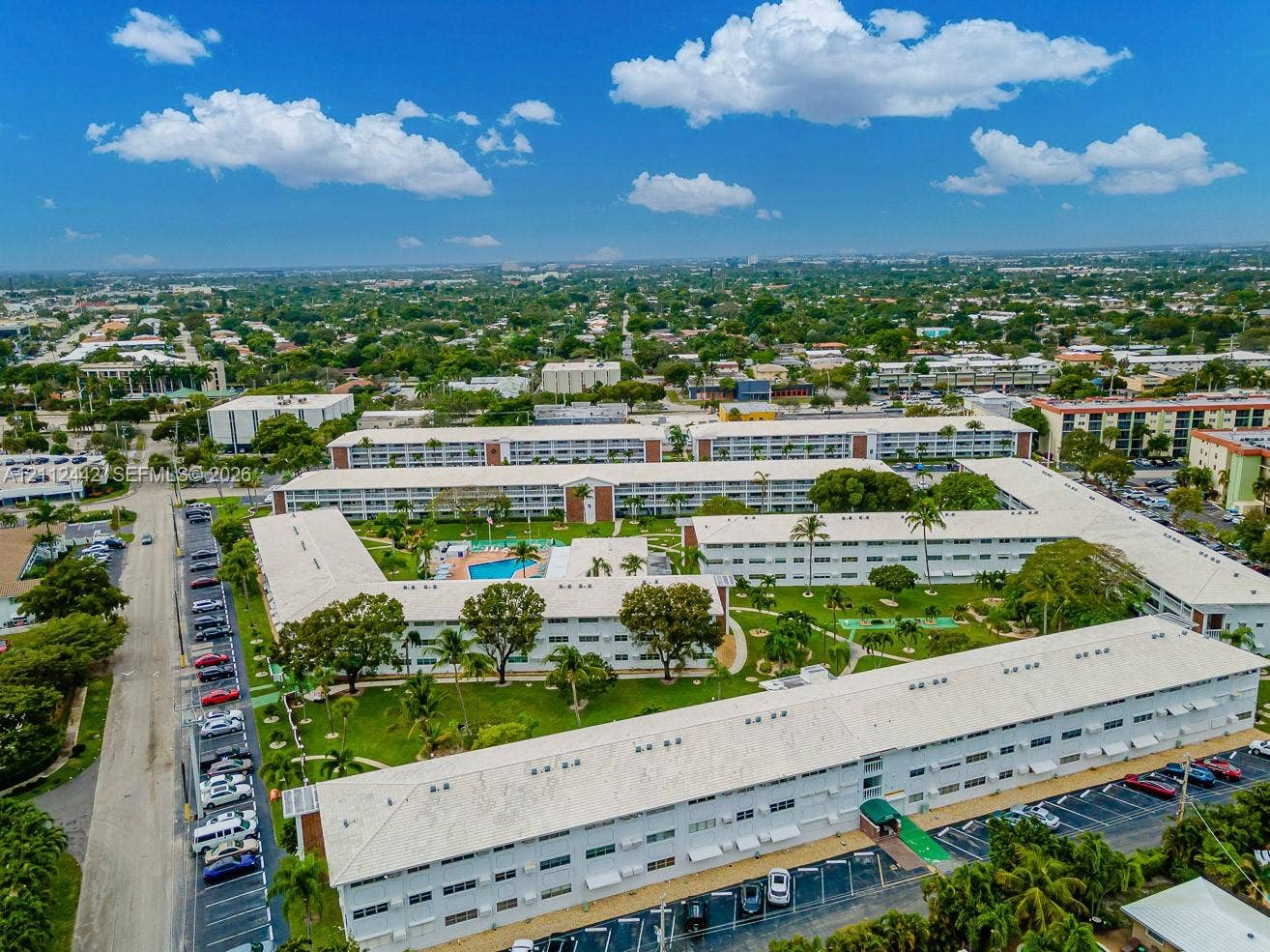 2455 NE 51st Street, #E114, Fort Lauderdale, FL 33308 Aerial perspective of a multi-building residential complex featuring a central courtyard, a swimming pool, mature landscaping, and dedicated surface parking