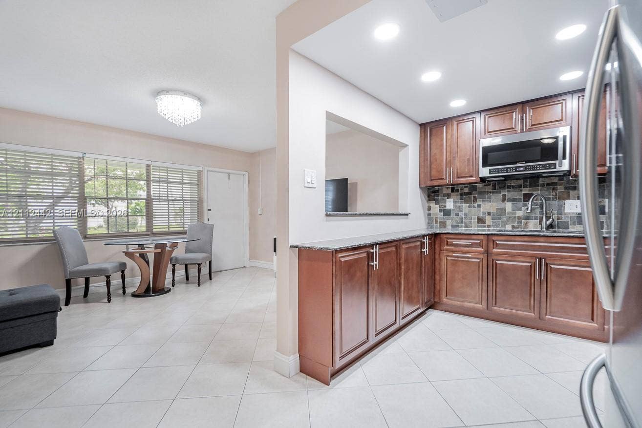 2455 NE 51st Street, #E114, Fort Lauderdale, FL 33308 Kitchen featuring wood cabinetry, stone-style mosaic tile backsplash, stone countertops, recessed lighting, and large-format tile flooring